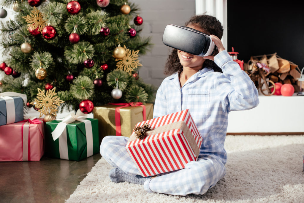 young girl looking into vr glasses while opening gifts near Christmas tree