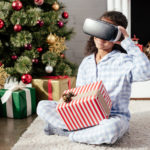 young girl looking into vr glasses while opening gifts near Christmas tree