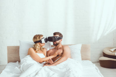 naked couple under white blanket using vr headsets