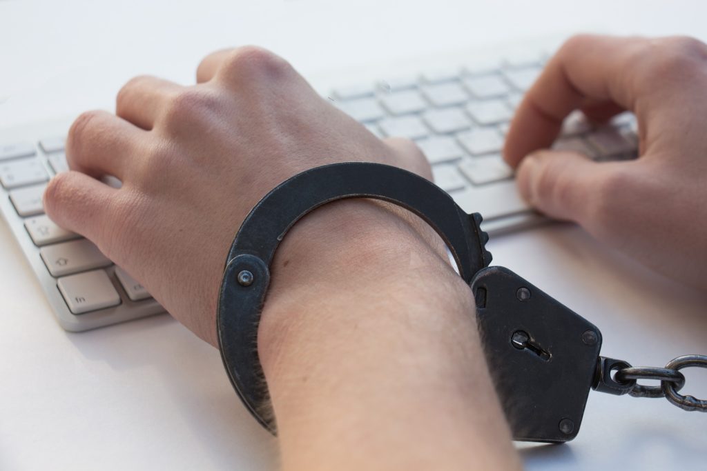 hands typing on keyboards with handcuffs