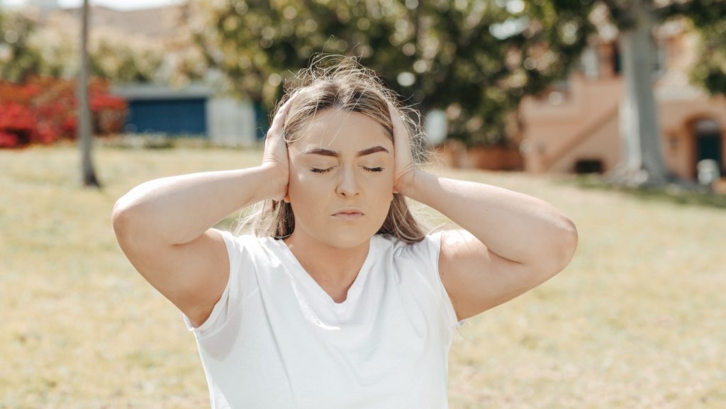 woman with closed eyes covering ears with hands