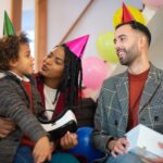 a couple with party hats looking at a boy holding a vr