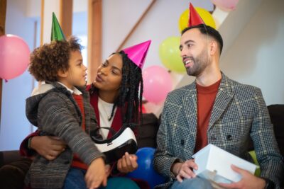 a couple with party hats looking at a boy holding a vr