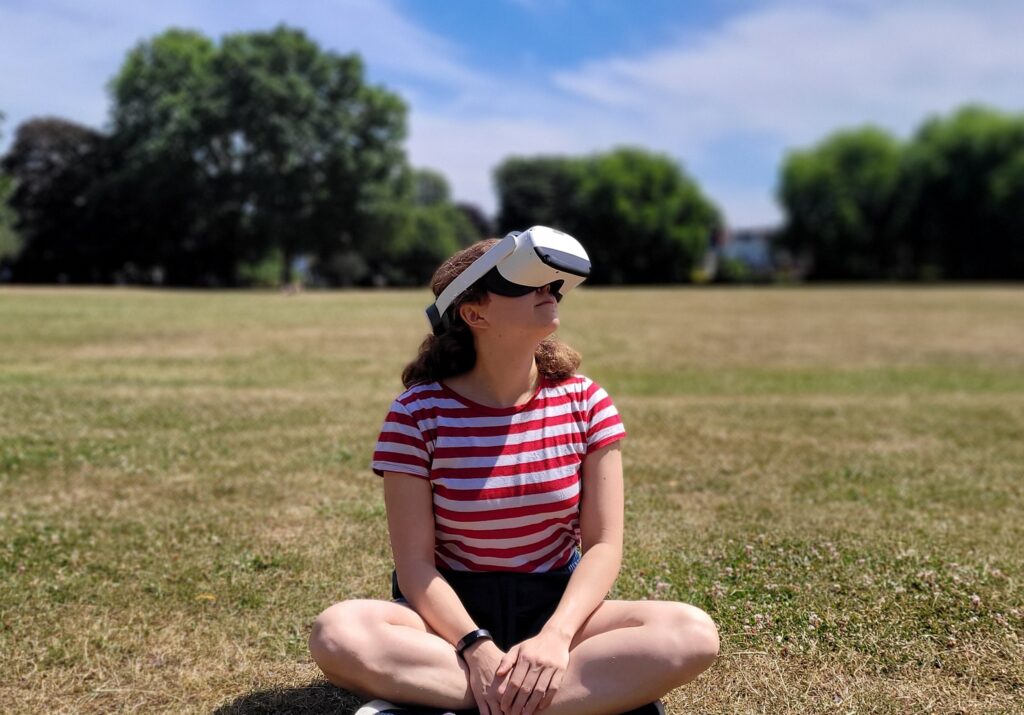 teen girl sitting on grass field wearing vr goggles